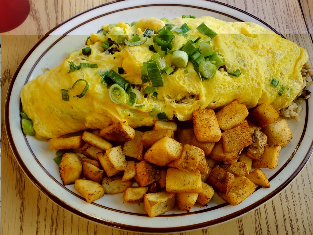 The Lolo Rick's Adobo Fried Rice. A large plate with the Adobo Fried Rice wrapped in egg with a large portion of breakfast potatoes at BabyStacks Cafe