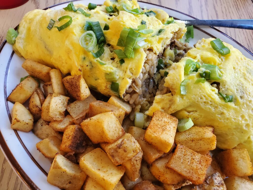 The Lolo Rick's Adobo Fried Rice. A large plate with the Adobo Fried Rice wrapped in egg cut in half with a large portion of breakfast potatoes